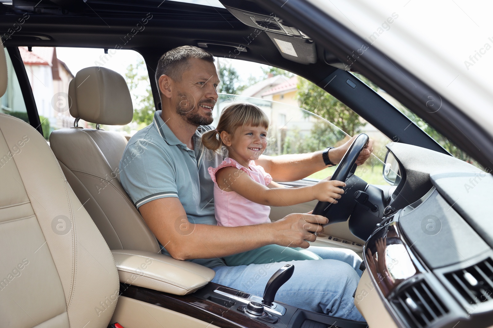 Photo of Happy man with his daughter holding steering wheel inside car