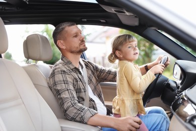 Photo of Man with his daughter holding steering wheel inside car