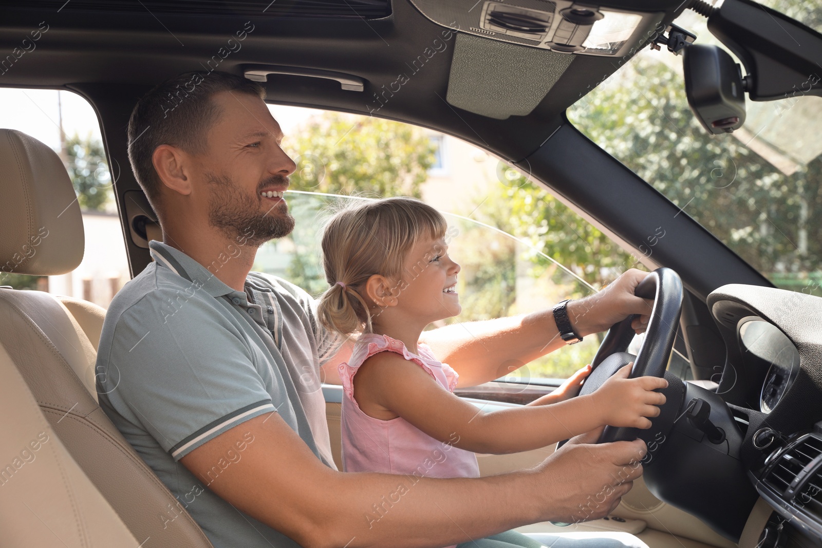 Photo of Man with his daughter holding steering wheel inside car