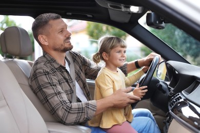 Happy man with his daughter holding steering wheel inside car