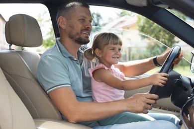 Photo of Happy man with his daughter holding steering wheel inside car