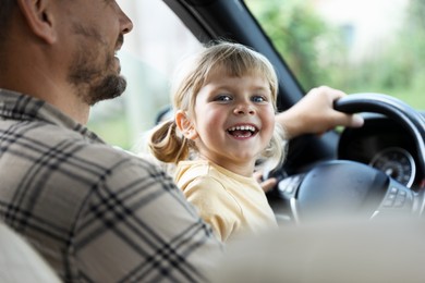 Photo of Man with his daughter holding steering wheel inside car, closeup