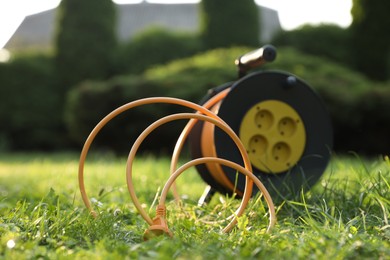 Photo of One extension cord reel on green grass outdoors, selective focus