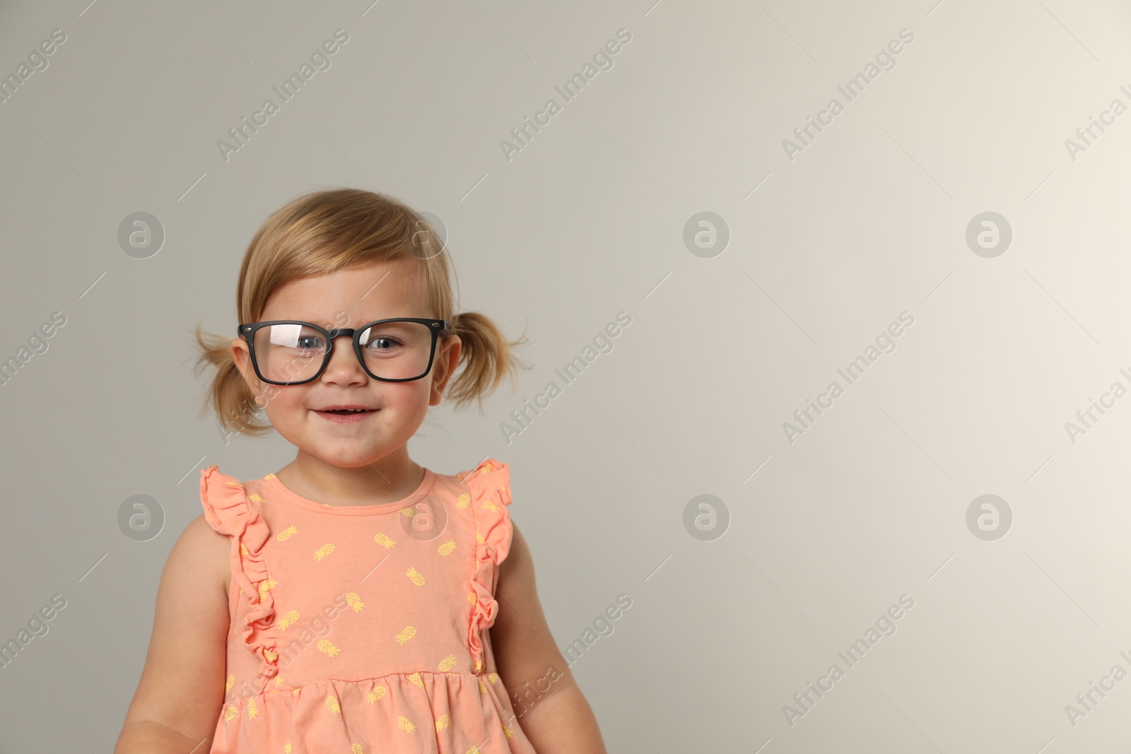 Photo of Cute little girl in glasses on light grey background. Space for text