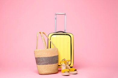 Yellow suitcase, wicker bag and shoes on pink background