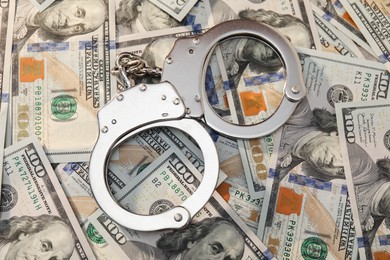 Handcuffs on pile of dollar banknotes, flat lay