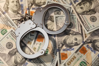 Handcuffs on pile of dollar banknotes, above view