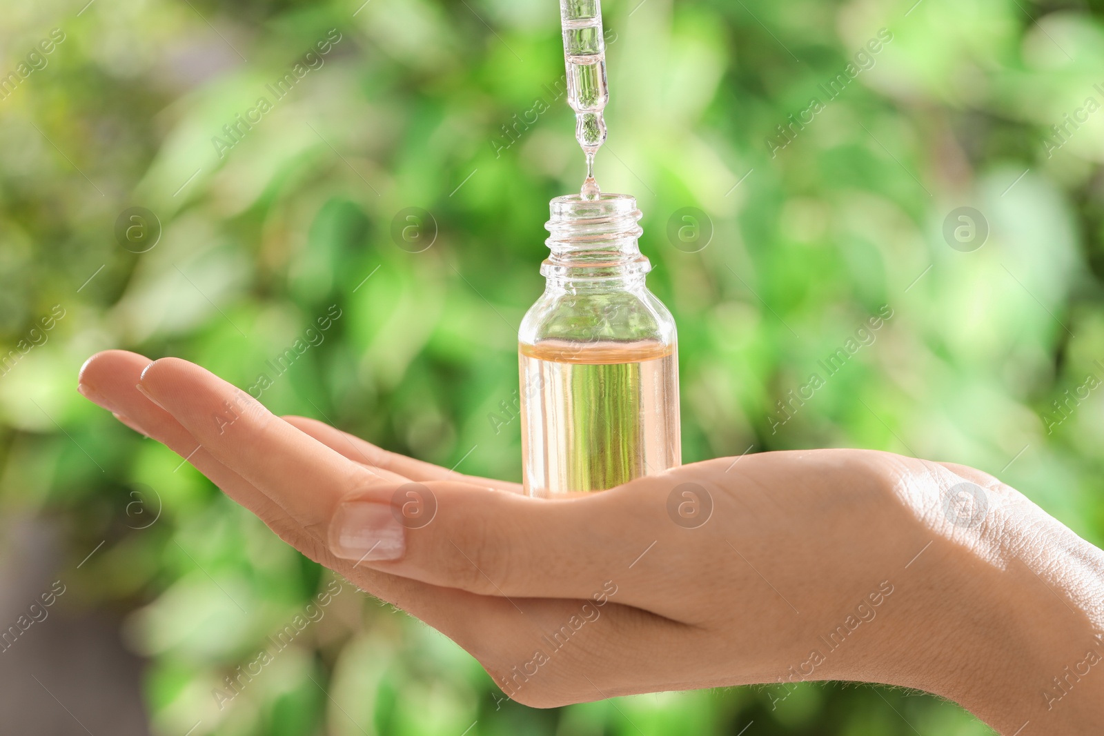 Photo of Woman dripping essential oil into bottle on blurred background, closeup