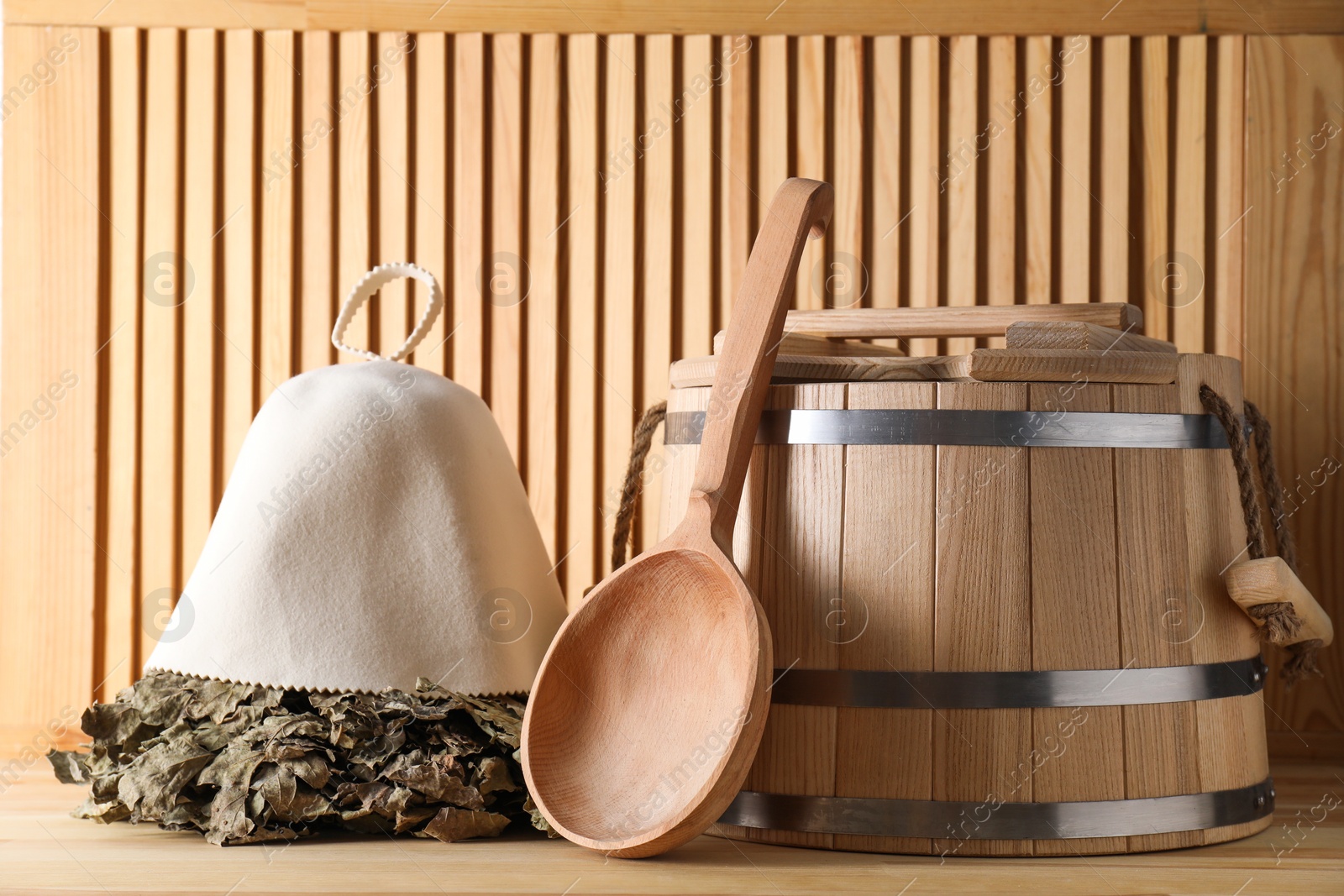 Photo of Oak sauna whisk, felt wool hat, bucket and ladle on wooden surface