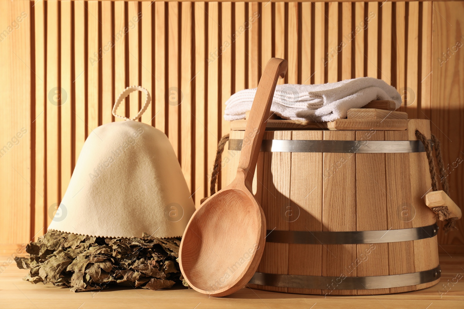 Photo of Oak sauna whisk, felt wool hat, towels, bucket and ladle on wooden surface