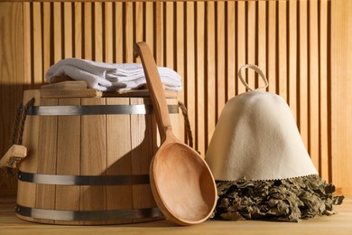 Photo of Oak sauna whisk, felt wool hat, towels, bucket and ladle on wooden surface