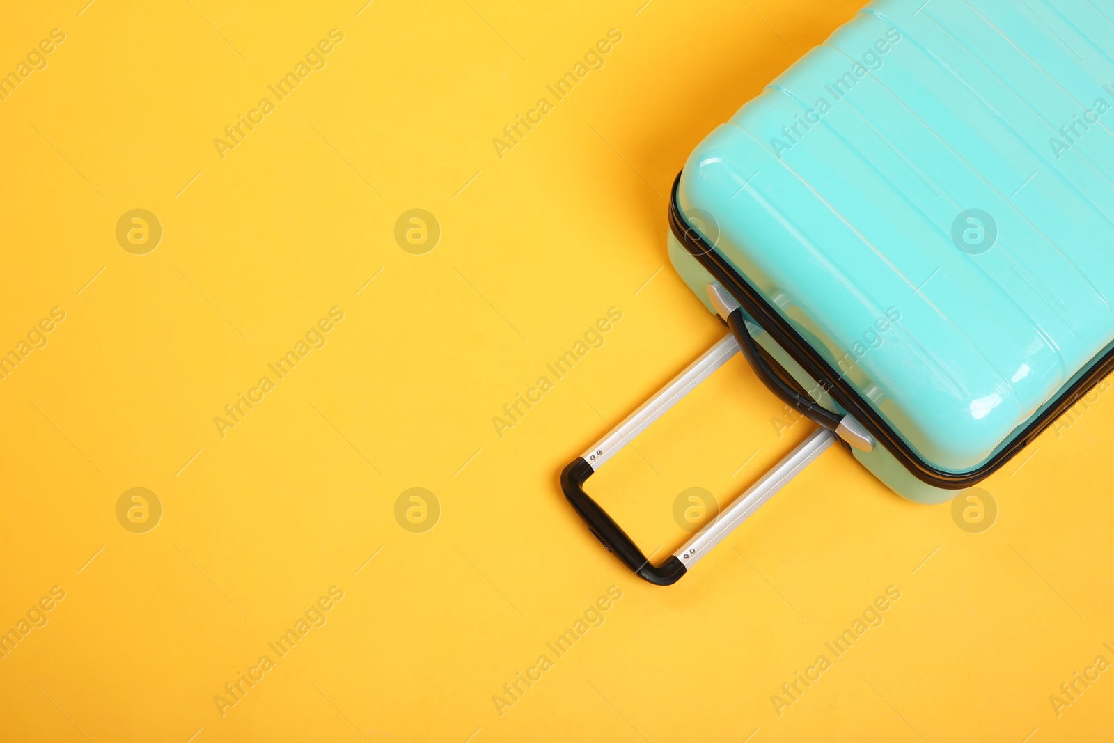 Photo of One turquoise suitcase on yellow background, above view. Space for text