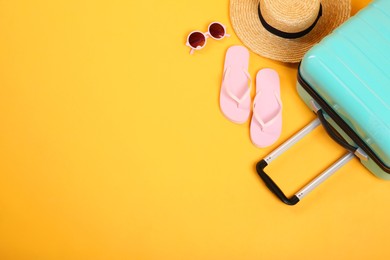 Photo of Turquoise suitcase, wicker hat, flip flops and sunglasses on yellow background, above view. Space for text