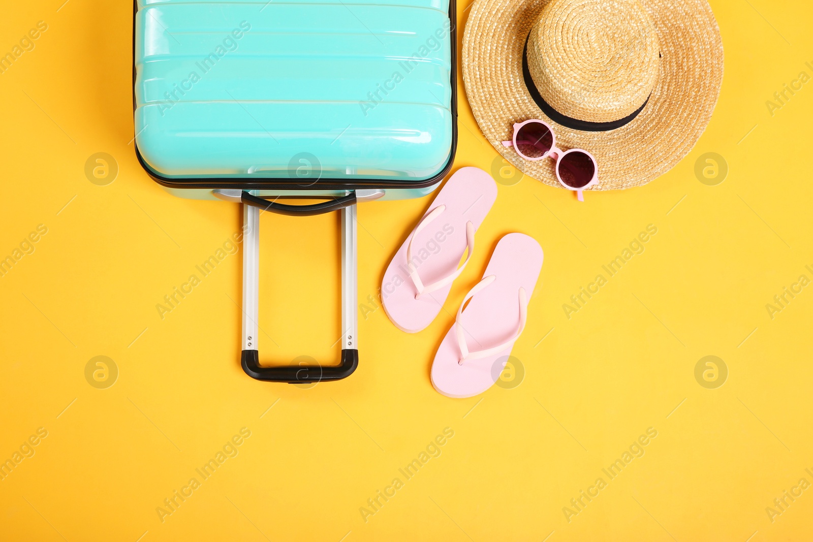 Photo of Turquoise suitcase, wicker hat, flip flops and sunglasses on yellow background, flat lay