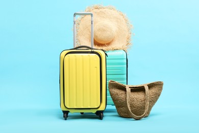 Suitcases with straw hat and bag on light blue background