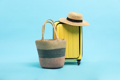 Photo of Yellow suitcase with wicker hat and bag on light blue background