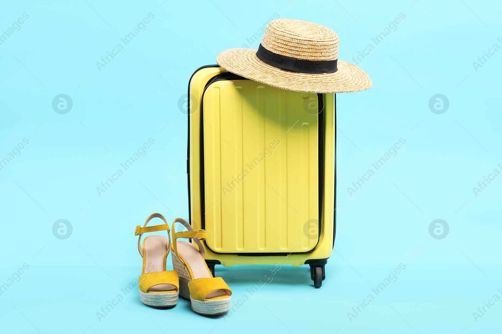 Photo of Yellow suitcase with shoes and wicker hat on light blue background