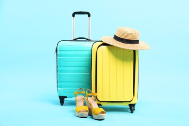 Photo of Suitcases with wicker hat and shoes on light blue background