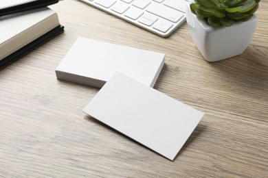 Photo of Blank business cards, plant and keyboard on wooden table. Mockup for design