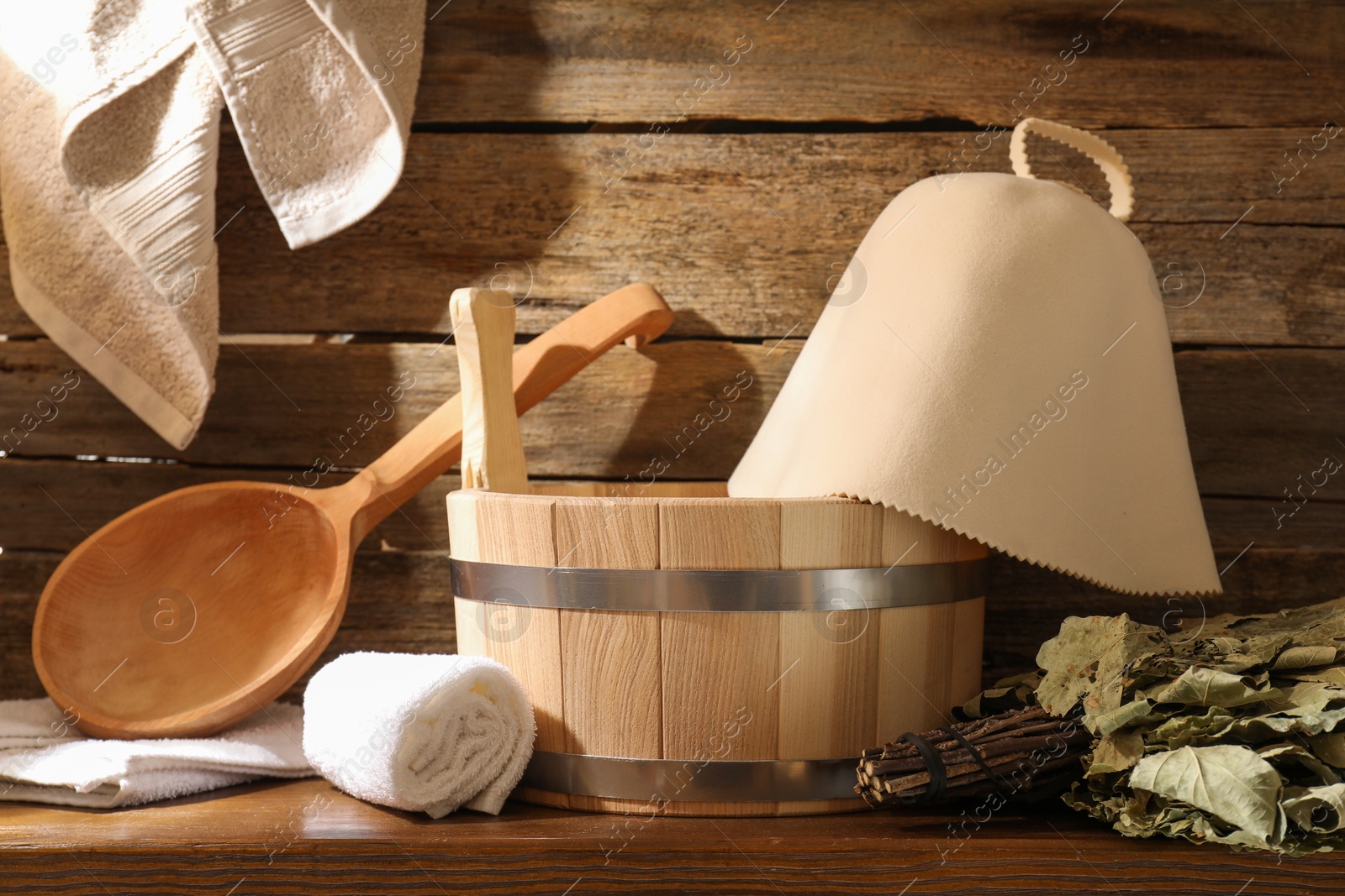 Photo of Sauna equipment. Bucket, ladle, felt wool hat, oak whisk and towels on wooden table indoors