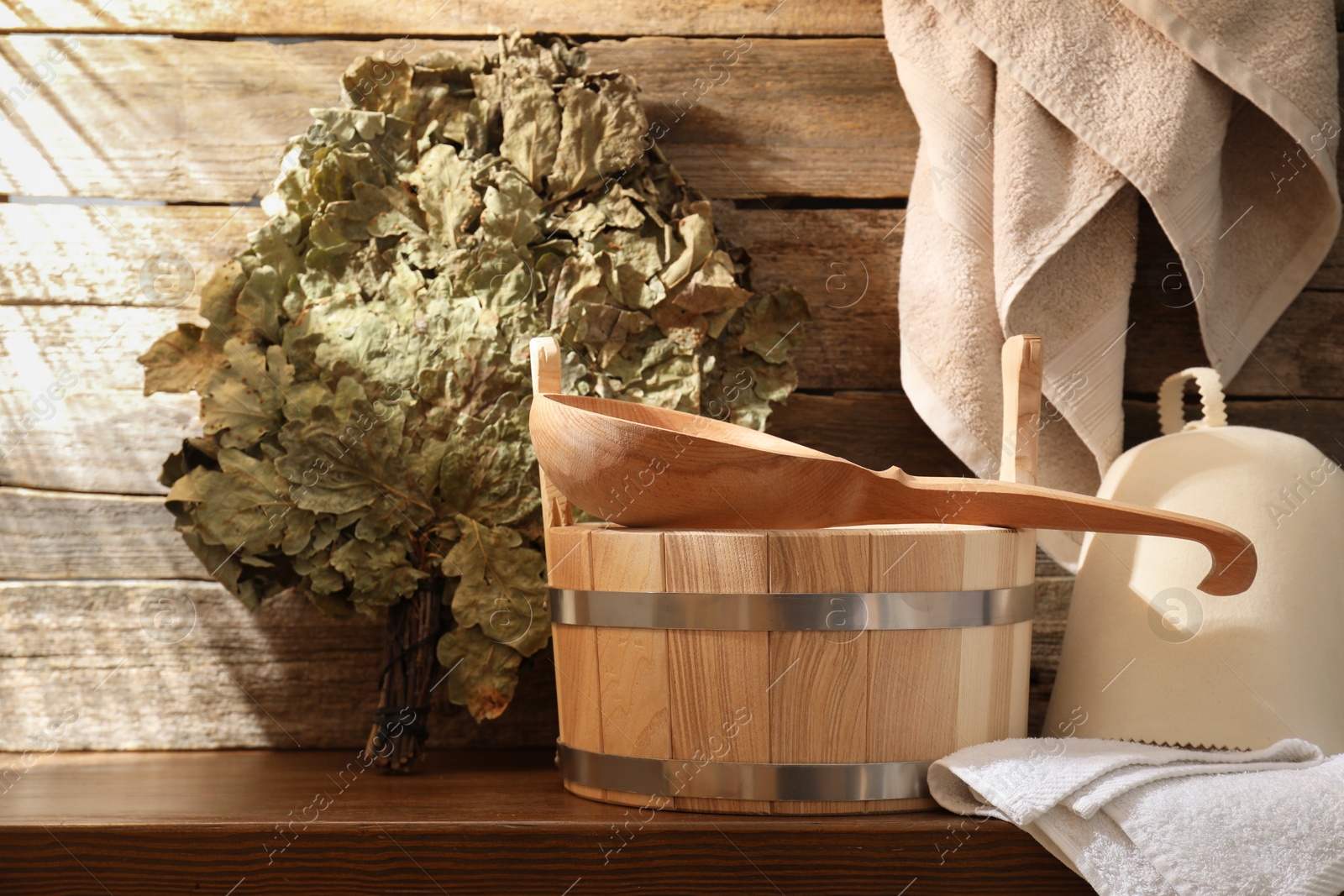 Photo of Sauna equipment. Bucket with ladle, felt wool hat, oak whisk and towels on wooden table indoors