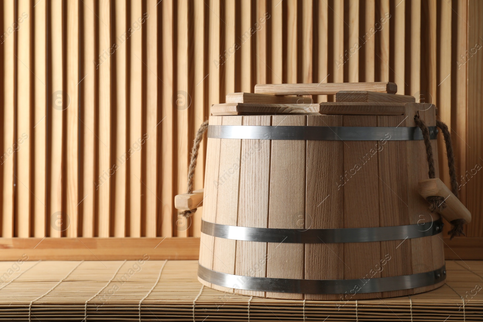 Photo of Sauna equipment. Bucket on bamboo bench near wooden wall, space for text