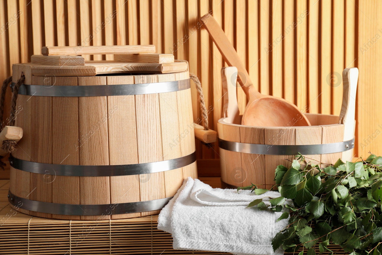 Photo of Sauna equipment. Buckets, birch whisk, ladle, and towel on bamboo bench near wooden wall