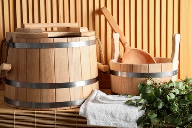 Sauna equipment. Buckets, birch whisk, ladle, and towel on bamboo bench near wooden wall