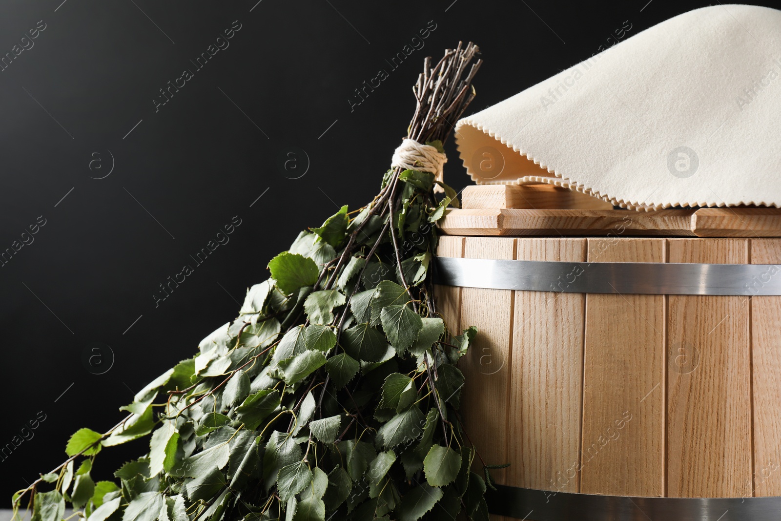 Photo of Sauna equipment. Bucket, birch whisk and felt wool hat on black background, closeup