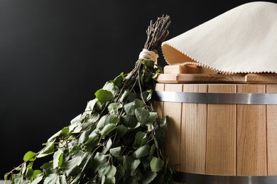 Photo of Sauna equipment. Bucket, birch whisk and felt wool hat on black background, closeup