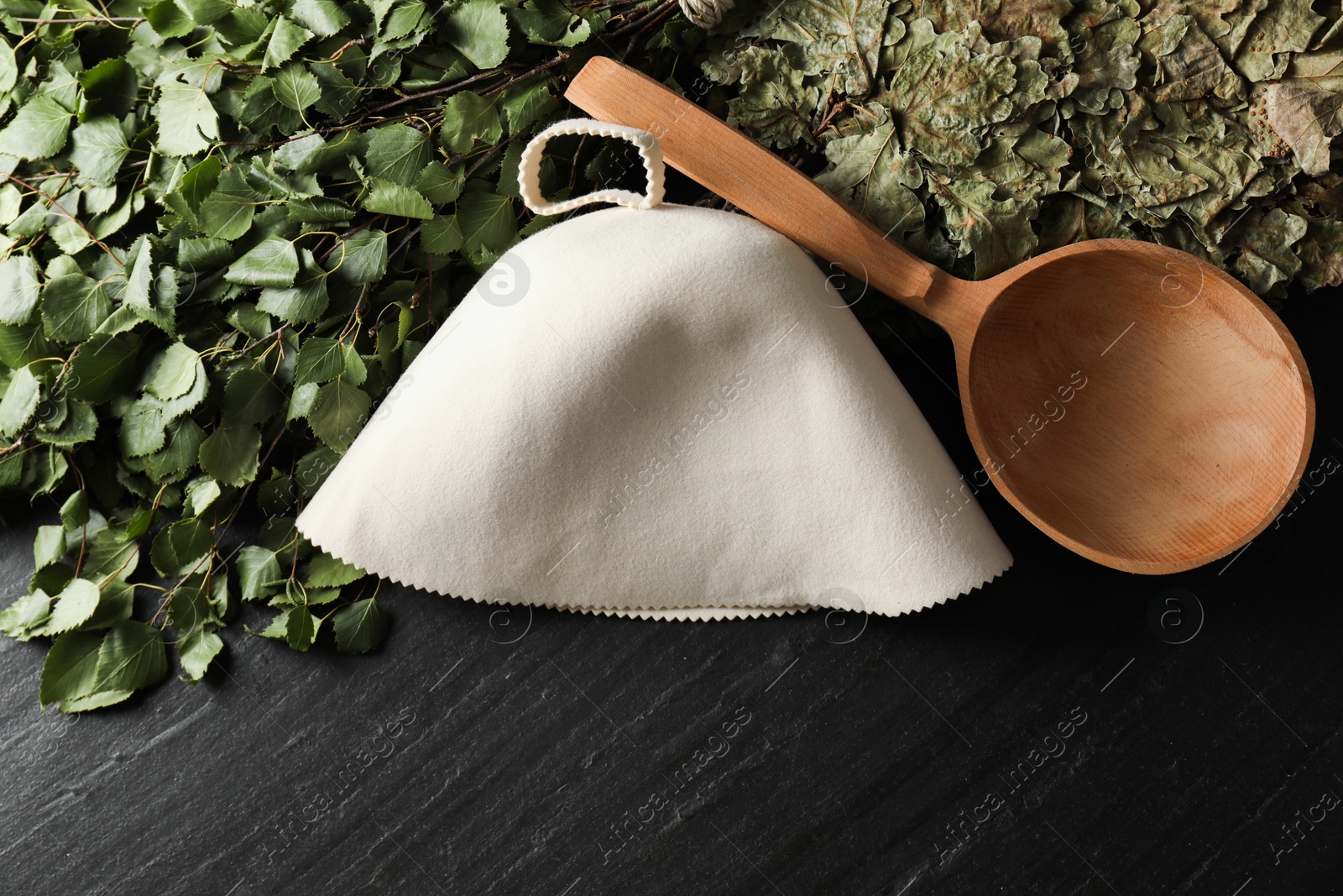 Photo of Sauna whisks, felt wool hat and ladle on black textured surface, flat lay