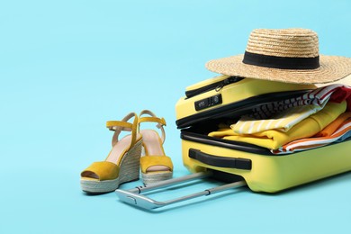 Photo of Yellow suitcase with clothes, shoes and wicker hat on light blue background