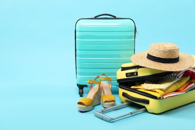 Photo of Suitcases with clothes, shoes and wicker hat on light blue background