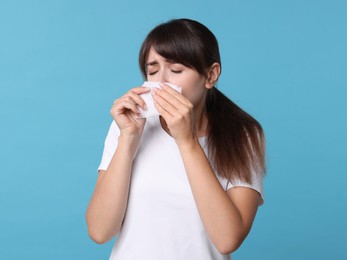 Photo of Woman with napkin suffering from sinusitis on light blue background