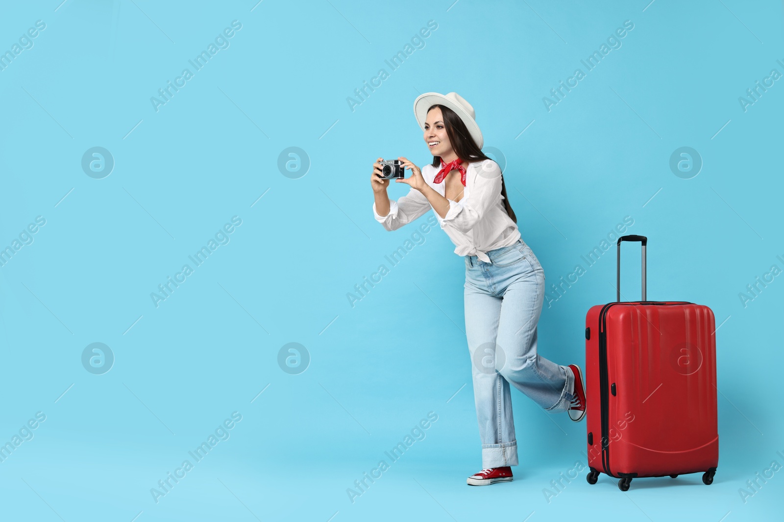 Photo of Happy young woman with suitcase and vintage camera on light blue background, space for text