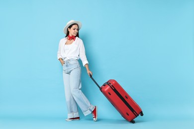 Happy young woman with suitcase on light blue background