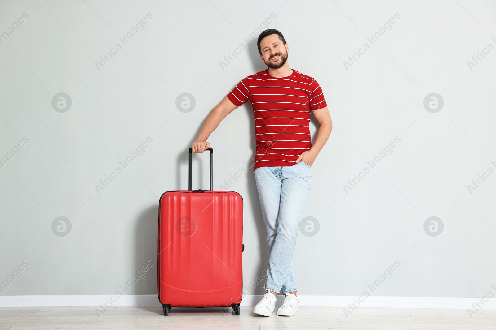 Photo of Happy man with suitcase near light gray wall indoors