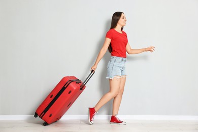 Happy young woman with suitcase walking indoors