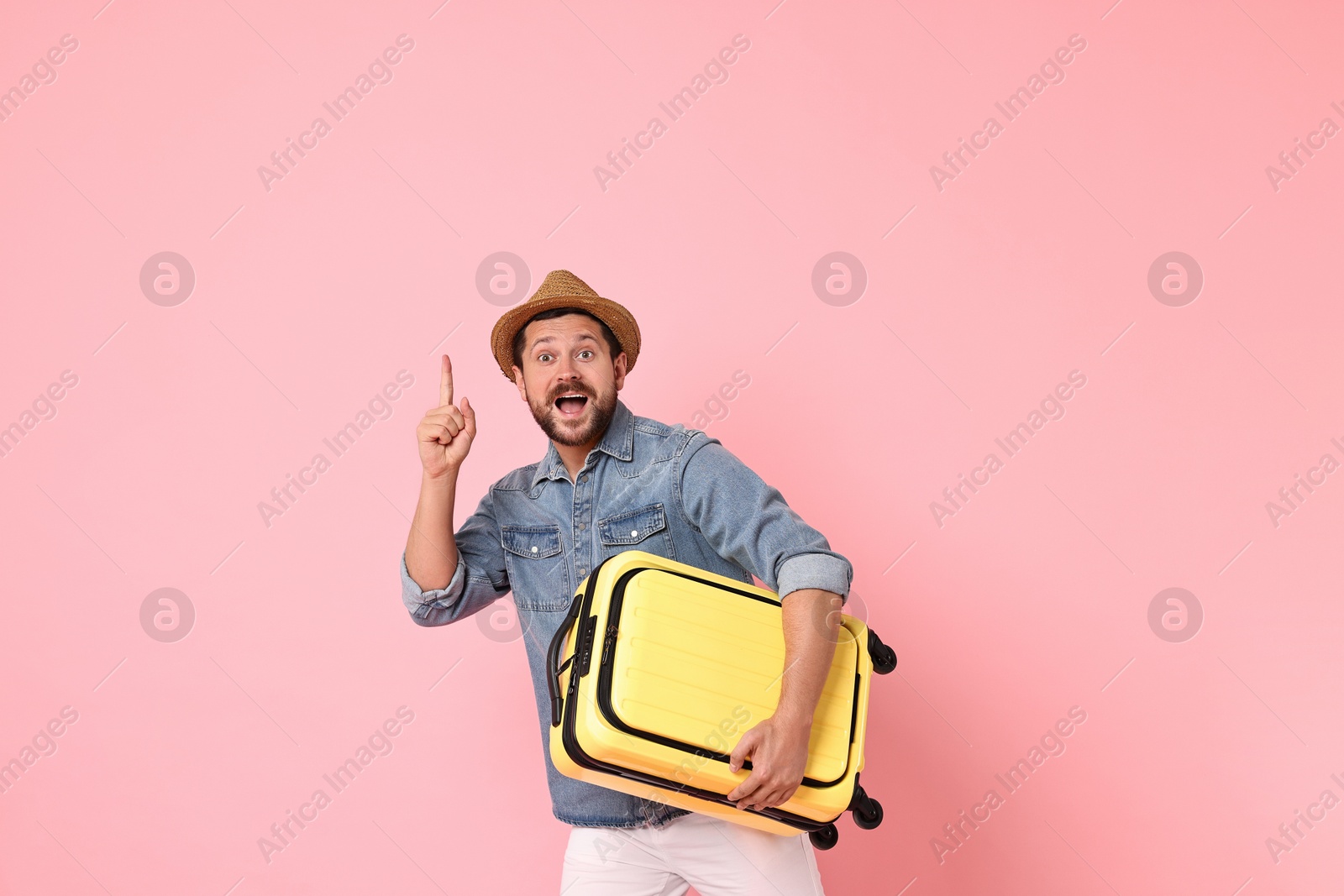 Photo of Happy man with suitcase pointing at something on pink background