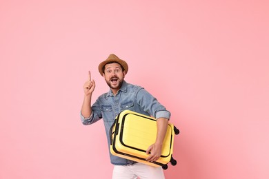 Photo of Happy man with suitcase pointing at something on pink background