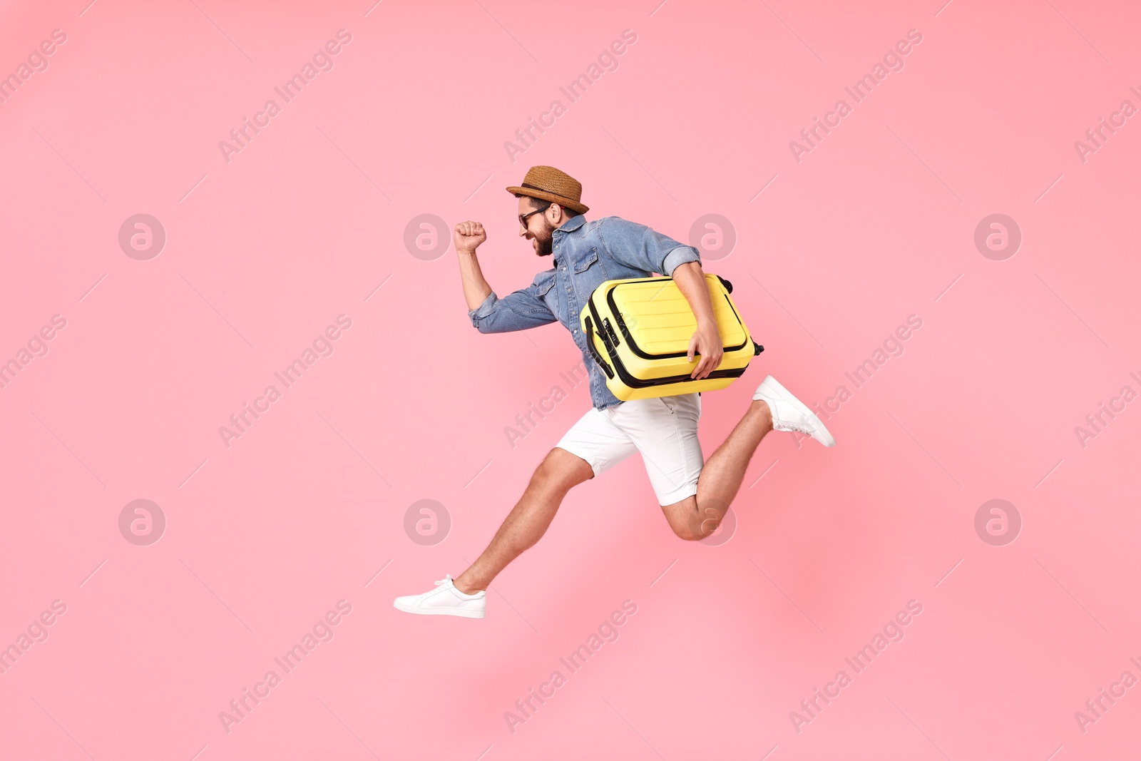 Photo of Happy man in sunglasses with suitcase jumping on pink background