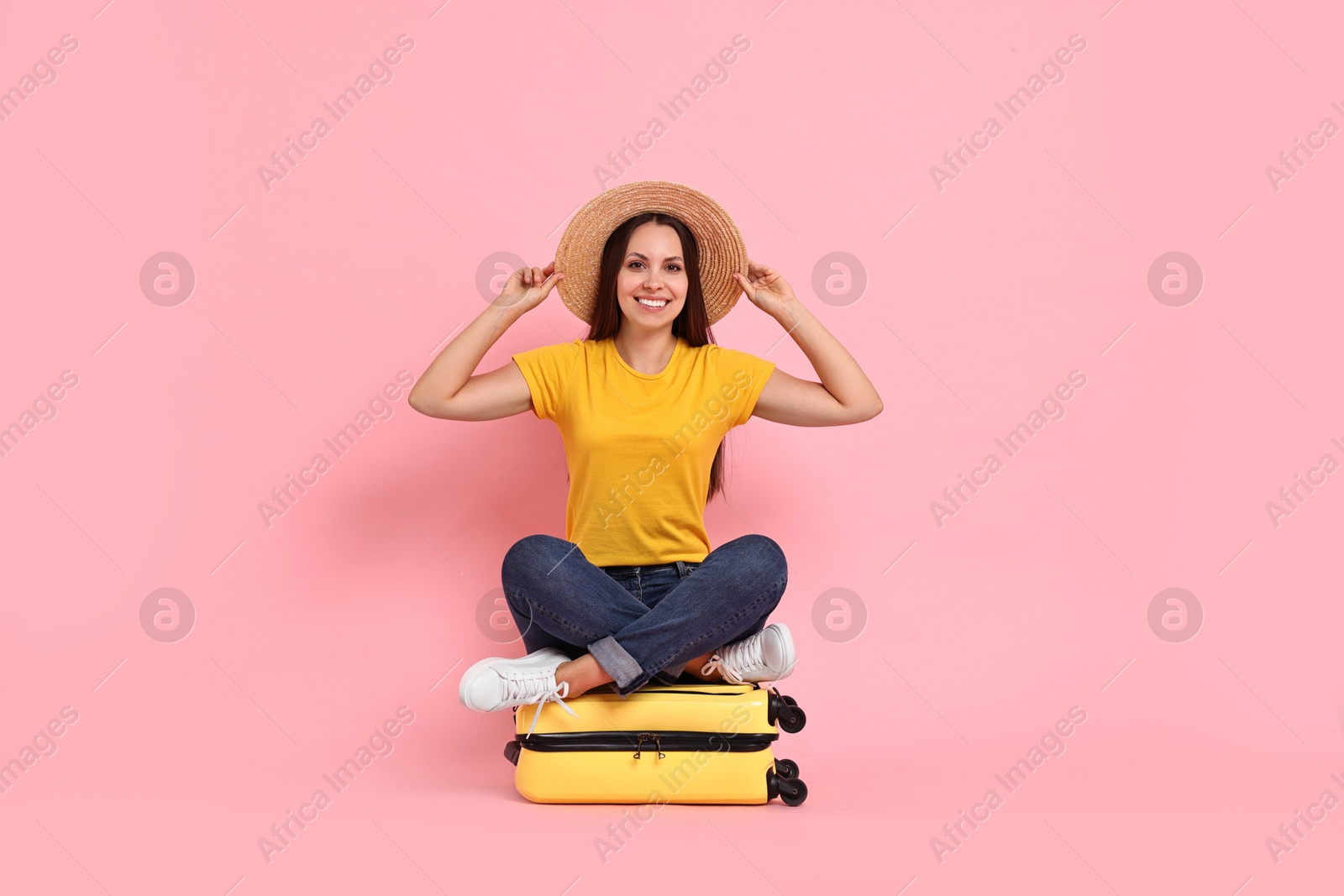 Photo of Happy young woman sitting on suitcase against pink background