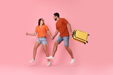 Photo of Happy woman and man with suitcase jumping on pink background