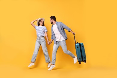 Photo of Happy man with suitcase and woman running on orange background