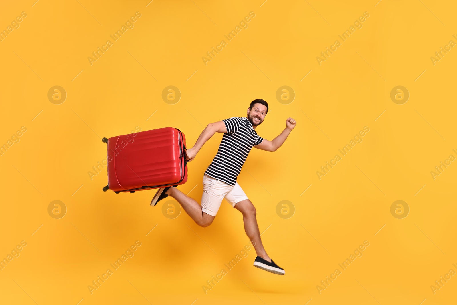 Photo of Happy man with suitcase running on orange background