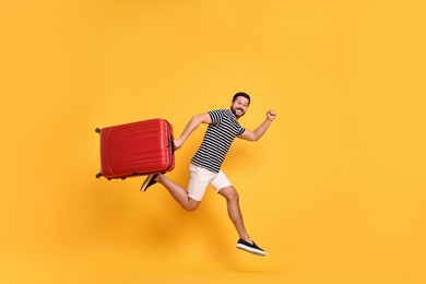 Happy man with suitcase running on orange background