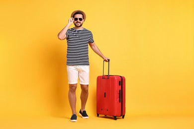 Photo of Happy man in sunglasses with suitcase on orange background