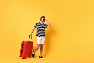 Photo of Happy man in sunglasses with suitcase walking on orange background