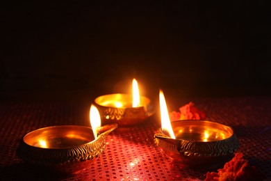 Photo of Diwali celebration. Diya lamps and beautiful flowers on dark background, closeup