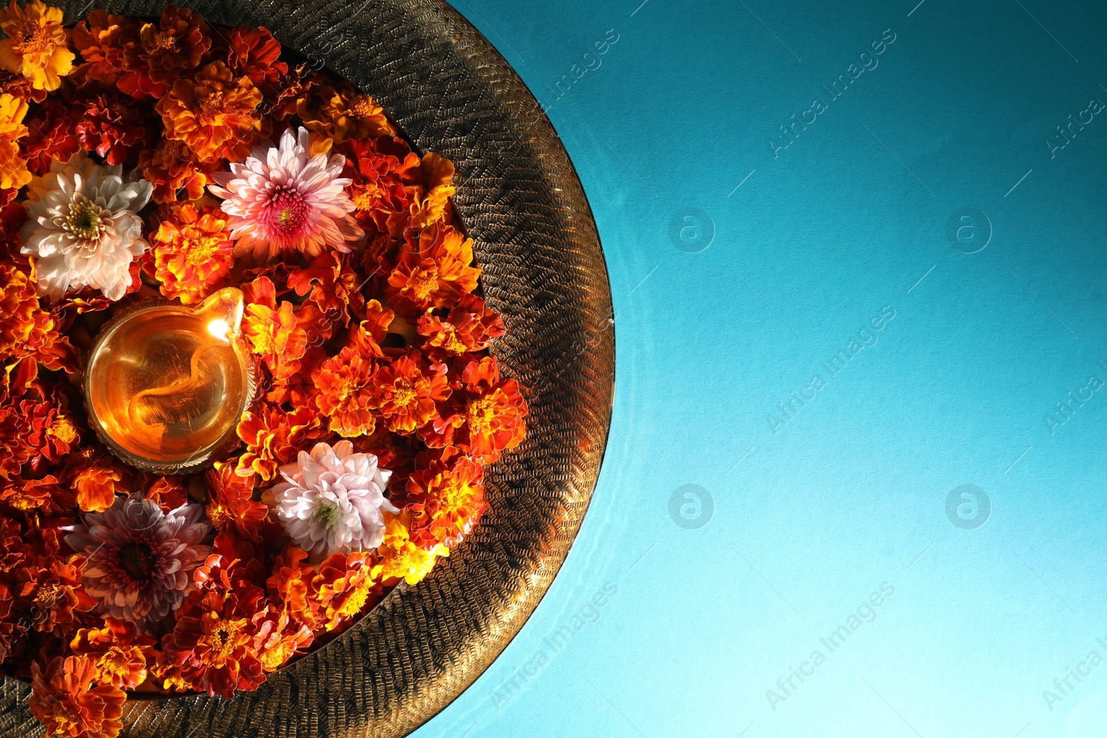 Photo of Diwali celebration. Diya lamp and beautiful flowers on turquoise background, top view. Space for text